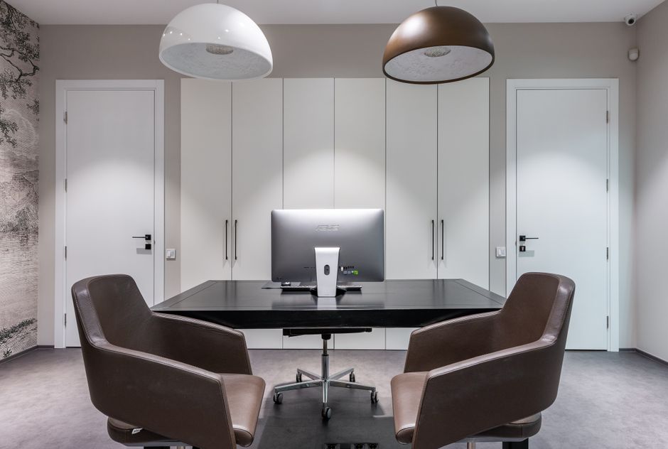 Agence immobilière : votre atout pour un projet réussi 2 Intérieur d'une agence immobilière moderne avec un agent discutant avec un client devant un grand écran affichant des biens immobiliers.